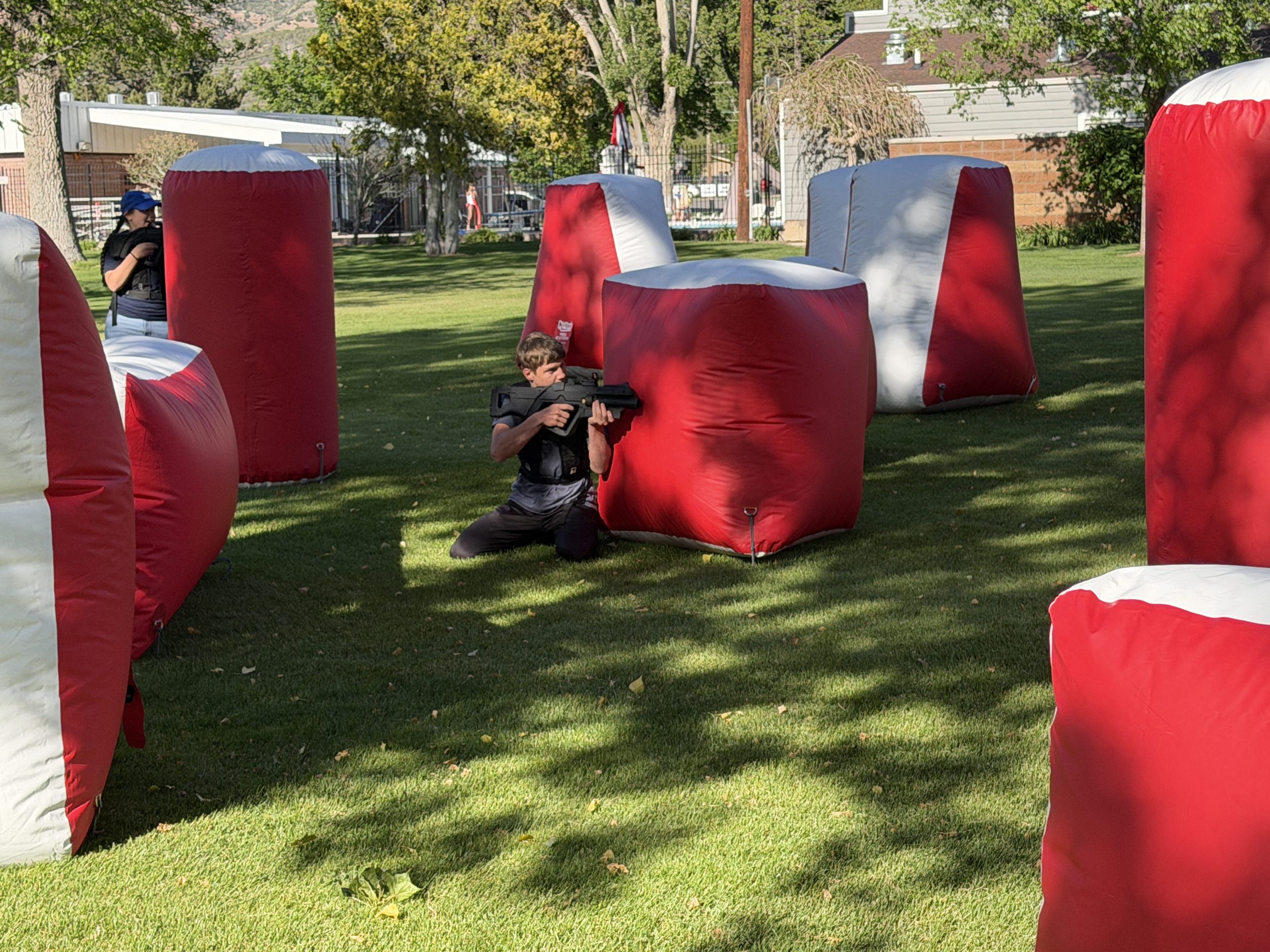 Players battling outside in a laser tag arena. One player kneeling by a bunker